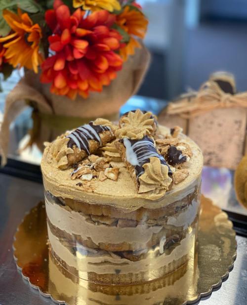 A layered cake topped with frosting, chocolate drizzle, and crushed cookies, alongside a bouquet of flowers.