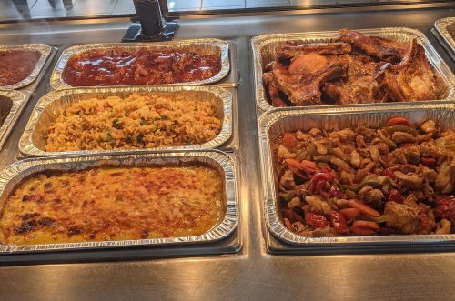 A display of various cooked dishes in aluminum trays, including rice, meats, and casseroles.