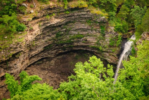 Aerial view of a lush green canyon with a waterfall cascading into a rocky basin below.