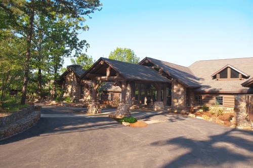 A rustic lodge with stone and wood architecture, surrounded by trees and a clear blue sky.