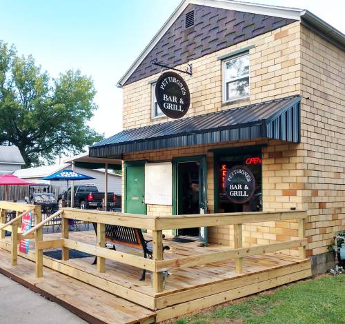 A two-story brick building with a sign reading "Pet Tibor's Bar & Grill," featuring a wooden deck and outdoor seating.
