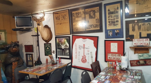 A cozy room with a wooden table, decorated walls featuring framed memorabilia, a mounted deer head, and a TV.