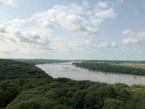 A scenic view of a river winding through lush green forests under a partly cloudy sky.