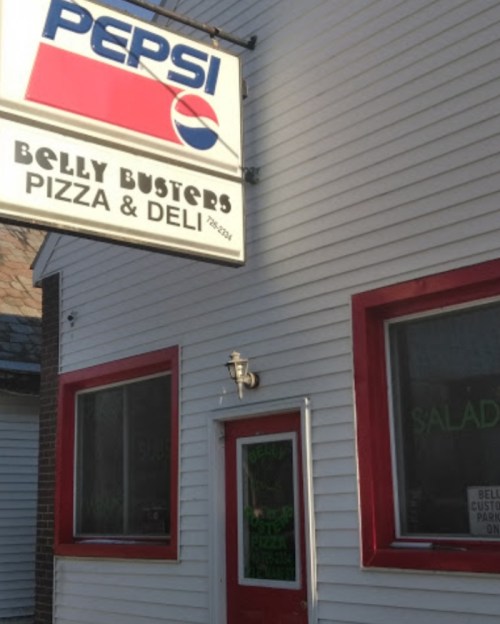 Exterior of Belly Busters Pizza & Deli, featuring a Pepsi sign and red-trimmed windows.