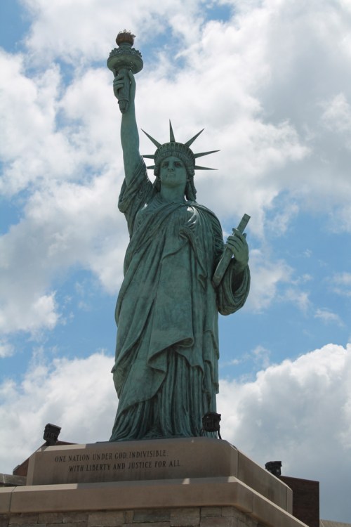 The Statue of Liberty stands tall against a cloudy sky, holding a torch and inscribed with a message of freedom.