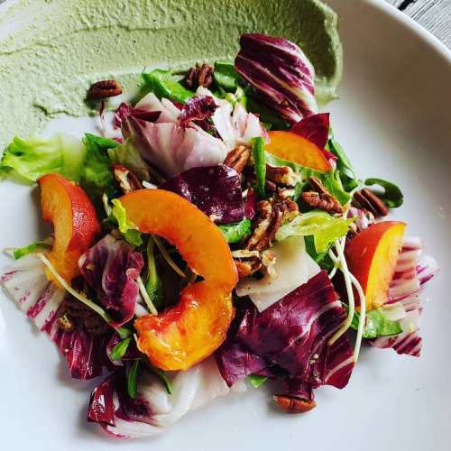 A colorful salad with mixed greens, orange slices, pecans, and a green dressing on the side.