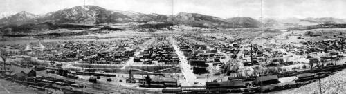 A panoramic black-and-white view of a historic town surrounded by mountains, featuring numerous buildings and streets.