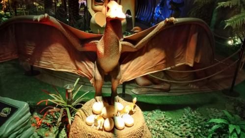 A dragon statue with outstretched wings stands over a nest of eggs in a lush, themed environment.