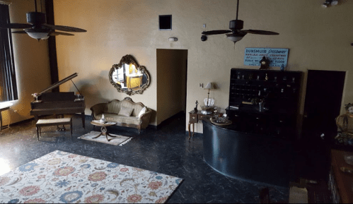 A spacious, vintage-style room with a piano, elegant furniture, and a decorative mirror, featuring dark flooring and ceiling fans.