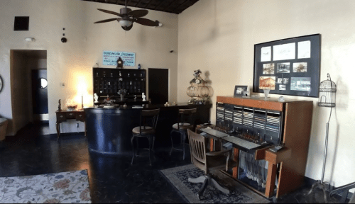 A cozy reception area with a dark wooden desk, chairs, and decorative items on the walls and shelves.