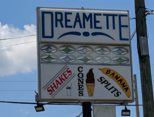 Sign for Dreamette featuring shakes, cones, and banana splits against a blue sky.