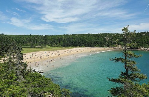 A scenic beach with people enjoying the sun, surrounded by lush greenery and clear turquoise water.