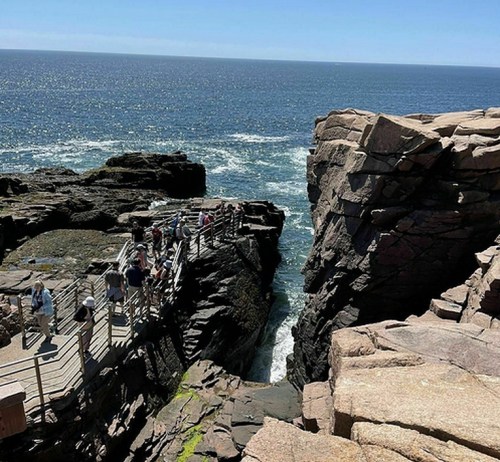 A rocky coastline with a wooden bridge connecting two cliffs, overlooking the ocean on a sunny day.