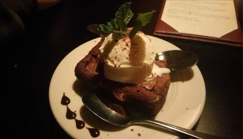 A warm chocolate dessert topped with vanilla ice cream and a mint leaf, served on a white plate with two spoons.