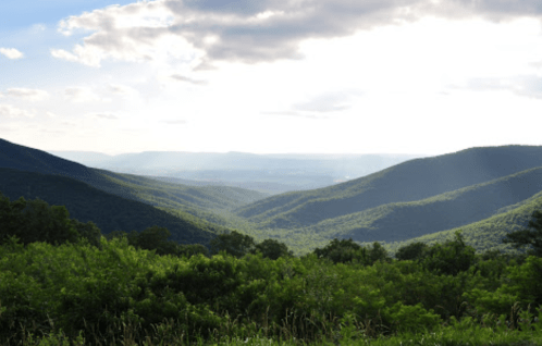 A scenic view of lush green mountains and valleys under a partly cloudy sky.