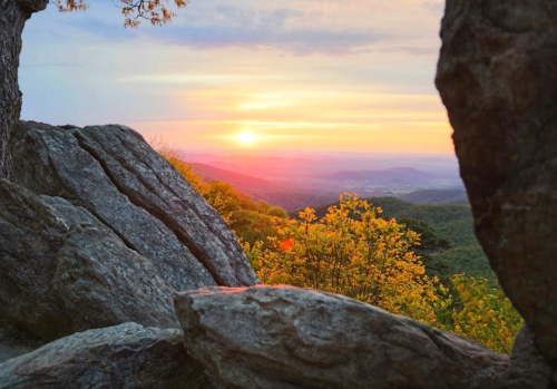 Sunset view through rocky formations, with vibrant colors illuminating the sky and surrounding trees.