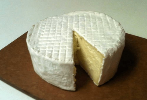 A round wheel of cheese with a white rind and a slice cut out, resting on a wooden board.