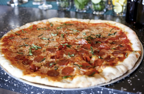 A large pepperoni pizza topped with fresh basil on a black speckled table.