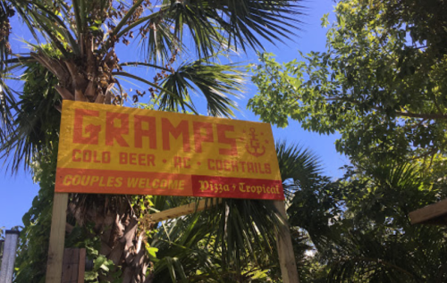 Sign for "Gramps" featuring cold beer and cocktails, surrounded by palm trees and a bright blue sky. Couples welcome.