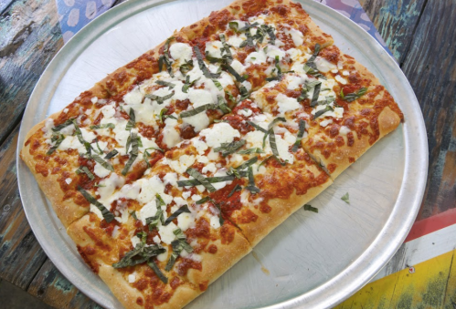 A rectangular pizza topped with tomato sauce, cheese, and fresh basil on a metal tray.