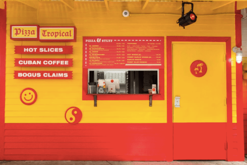 Brightly colored pizza stand with a menu, featuring items like hot slices and Cuban coffee. Red and yellow decor.