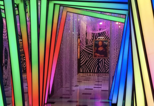 Colorful, illuminated frames create a vibrant entrance to a gallery featuring a classic painting and abstract patterns.