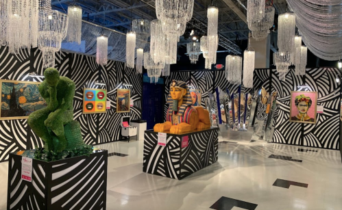 Art gallery featuring colorful sculptures and paintings against a bold black and white striped backdrop.