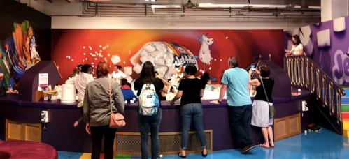 A colorful candy shop with customers at the counter, surrounded by vibrant murals and a playful atmosphere.