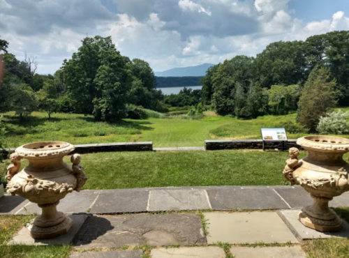 A scenic view of a lush landscape with a lake in the distance, framed by decorative stone planters.