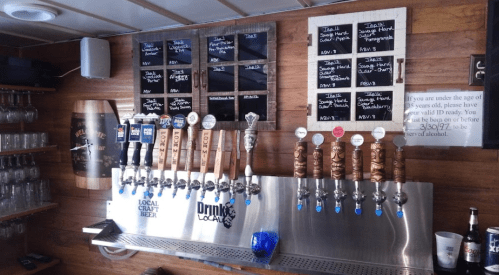 A wooden bar with a variety of beer taps and a chalkboard menu displaying drink options.