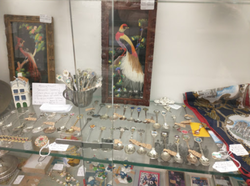 Display case filled with various vintage jewelry and decorative items, including spoons and framed artwork.