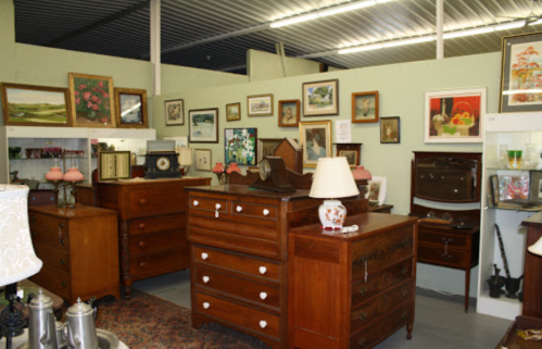 A vintage shop interior featuring wooden dressers, framed artwork, and decorative lamps on display.