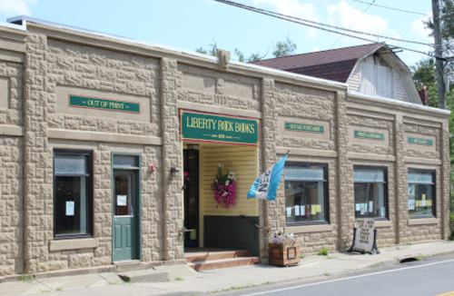 A stone building with a sign reading "Liberty Rock Banks," featuring a wreath and a blue flag outside.
