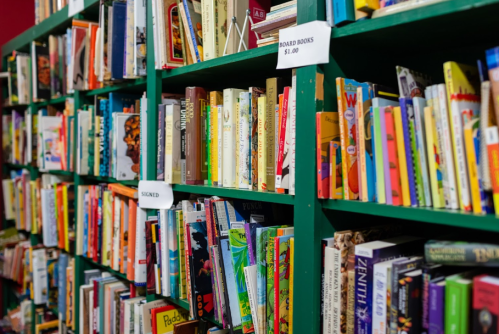 A colorful bookshelf filled with various books, including a sign for signed and board books priced at $1.00.