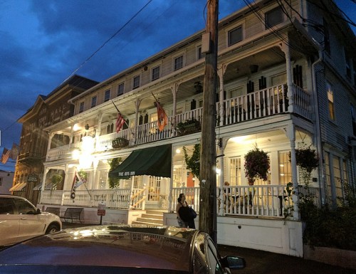 A historic building with multiple balconies, lit up at dusk, featuring flags and hanging plants.