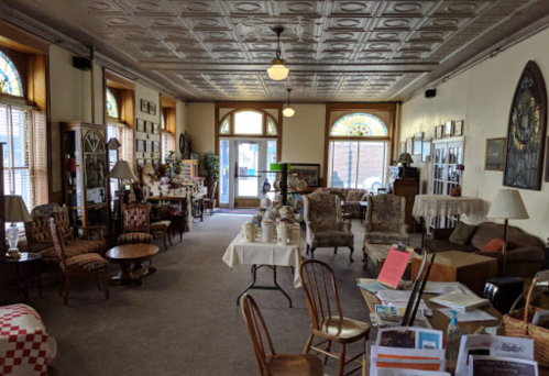 Cozy interior of a vintage shop with antique furniture, decorative items, and large windows letting in natural light.