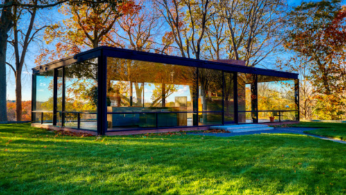 Modern glass house surrounded by colorful autumn trees and green grass, reflecting the vibrant landscape.