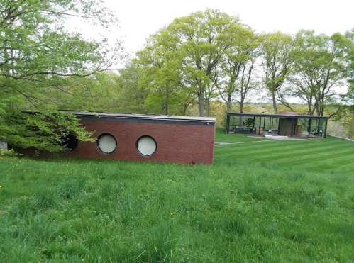 A modern building with circular windows sits in a lush green landscape, surrounded by trees and a manicured lawn.