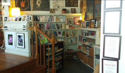 Cozy bookstore interior with wooden stairs, shelves filled with books, and art on the walls. Warm lighting enhances the atmosphere.