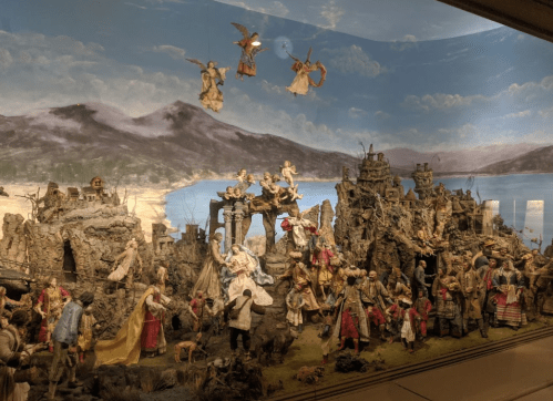 A detailed diorama depicting a historical scene with figures, buildings, and a scenic backdrop of mountains and water.
