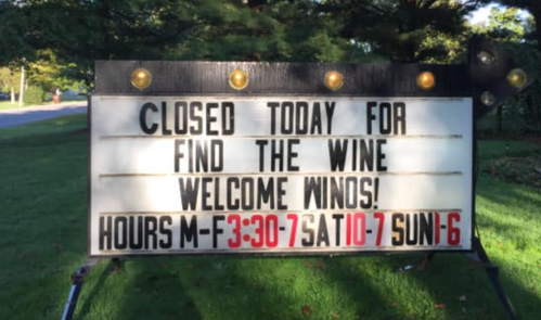 Sign announcing closure for "Find the Wine" event, welcoming wine enthusiasts, with business hours listed.