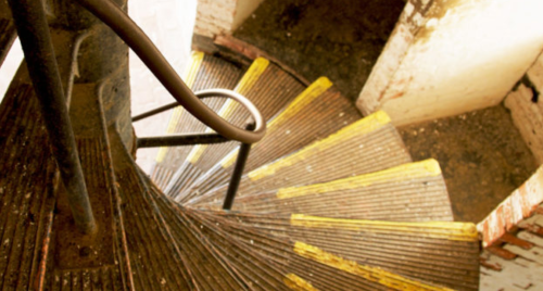 A spiral staircase with worn steps and yellow markings, viewed from above.