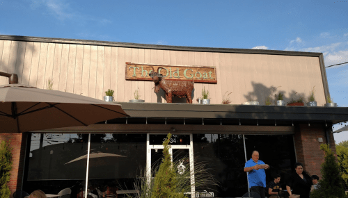 Exterior of "The Old Goat" restaurant with a decorative goat statue on the roof and outdoor seating below.