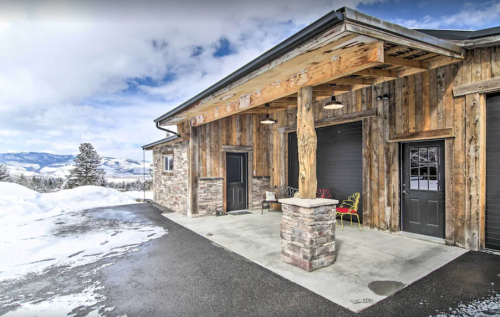 A rustic wooden house with stone accents, featuring a covered porch and snowy landscape in the background.
