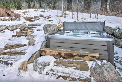A hot tub surrounded by snow-covered rocks and steps in a winter landscape.