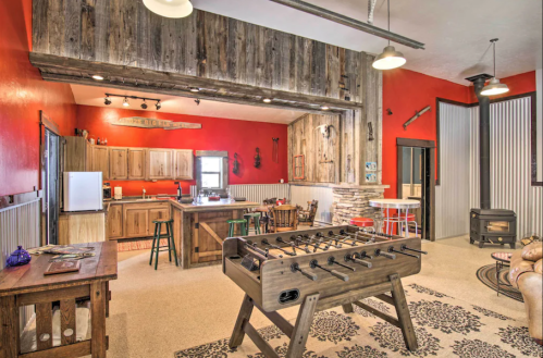 Cozy rustic interior with a red accent wall, wooden furniture, and a foosball table in a spacious living area.
