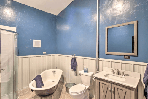 A modern bathroom featuring a blue wall, a freestanding tub, a shower, a toilet, and a sink with a mirror.