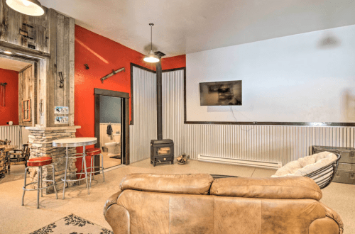 Cozy living space with a leather sofa, bar stools, and a wood stove, featuring rustic decor and a large TV.