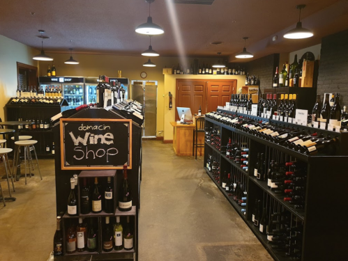Interior of a wine shop featuring shelves of wine bottles, a chalkboard sign, and a counter in the background.