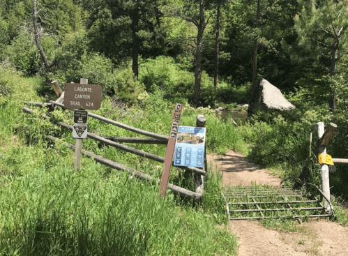 Trailhead entrance with signs for Lagunita Canyon Trail, surrounded by lush greenery and a wooden fence.